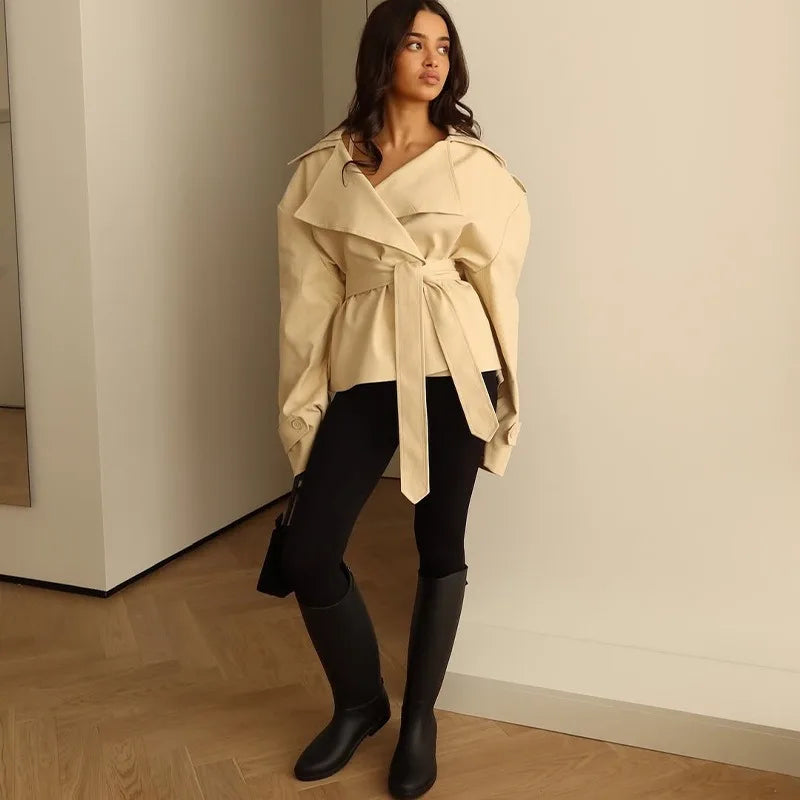 Woman wearing a beige trench coat and black boots in an indoor setting