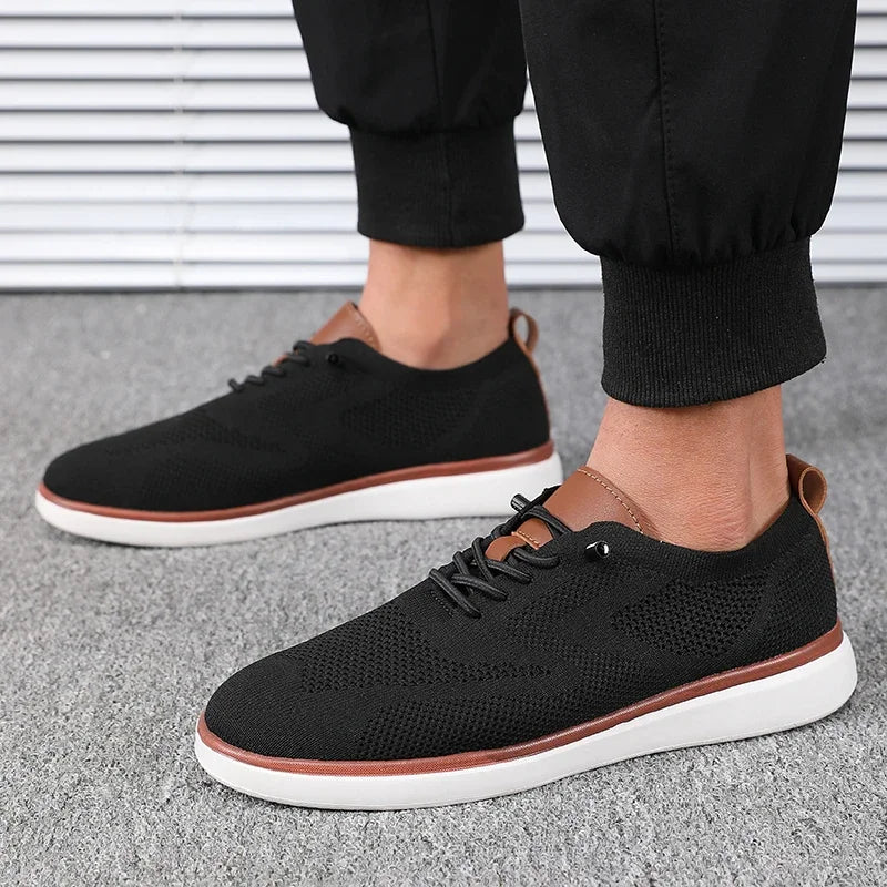 Black sneakers with white soles worn by a person on a gray pavement.