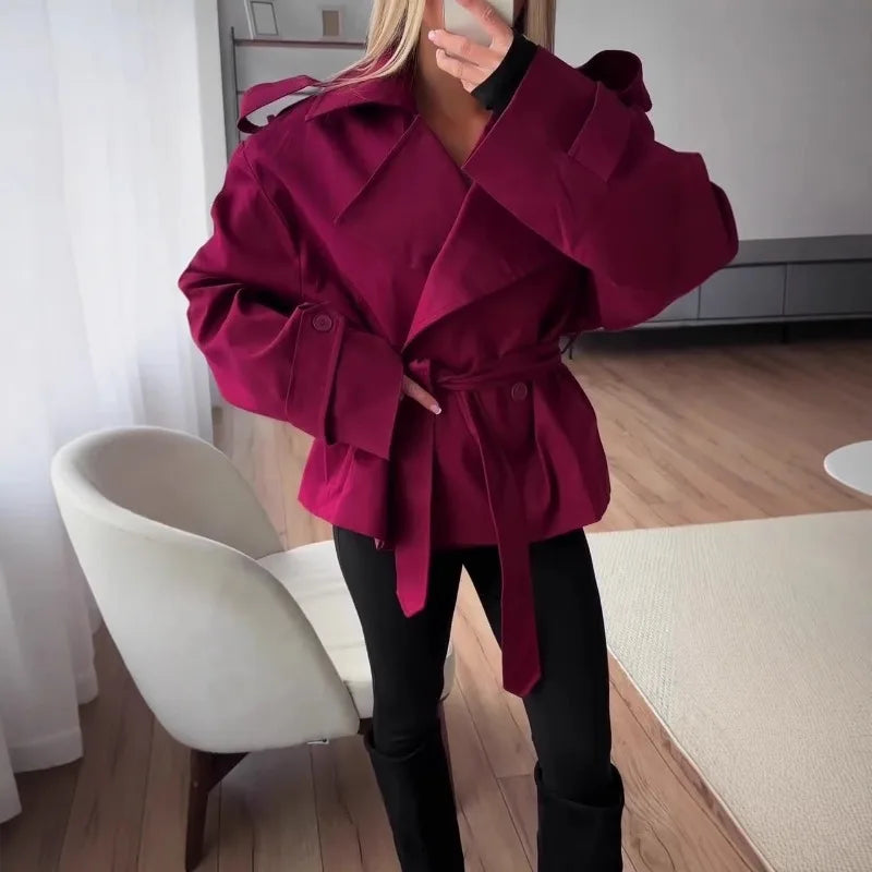 Person wearing a magenta coat in a room with a chair and white curtains.