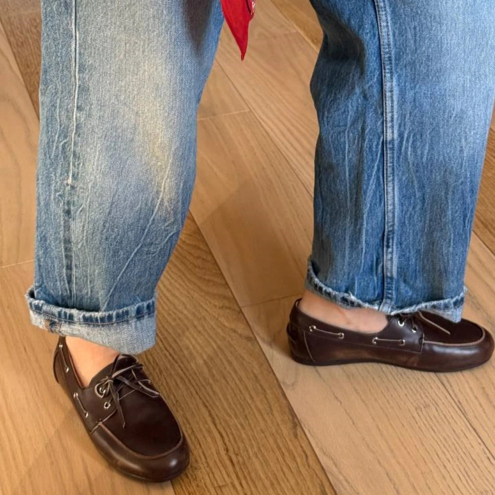 Brown loafers worn with blue jeans on a wooden floor
