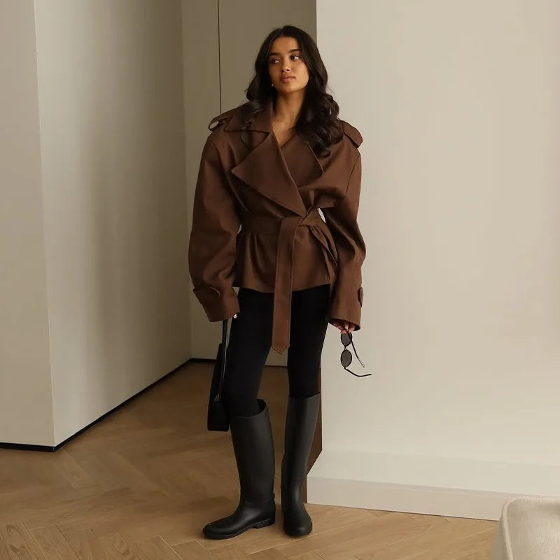Woman wearing a brown coat and black rain boots indoors.